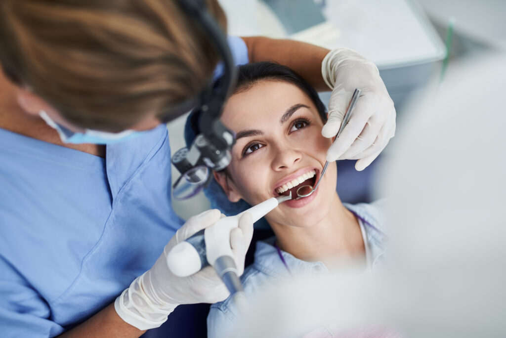 Top view portrait of beautiful lady with opened mouth sitting in dentist chair while stomatologist in sterile gloves doing professional teeth cleaning
