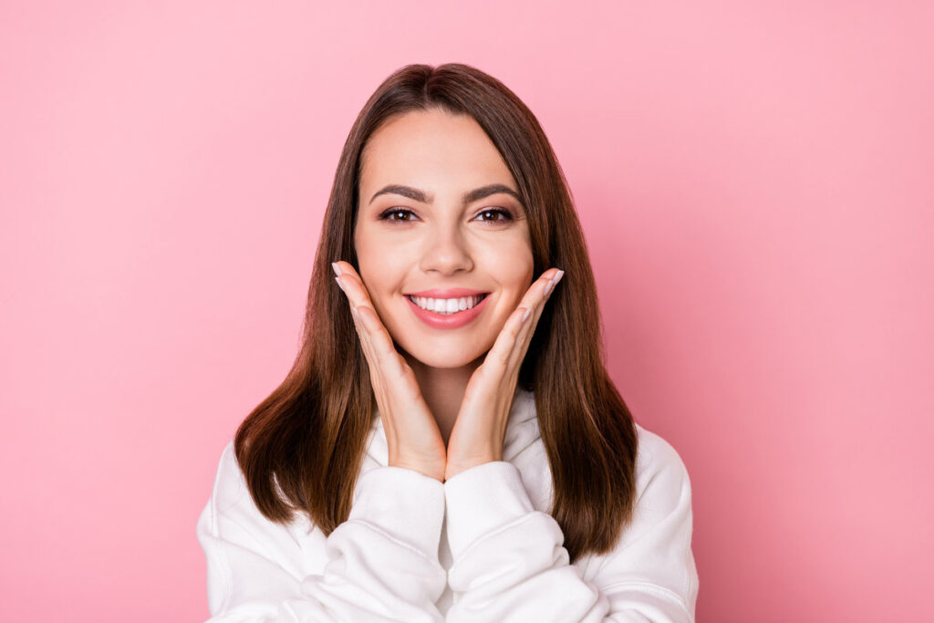 Photo of attractive happy young pretty woman hold hands face cheeks teeth isolated on pink color background.