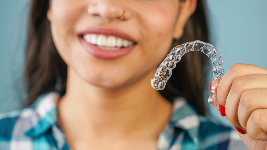 Young Asian Indian woman holding removable invisible aligner, also known as invisalign or clear aligner