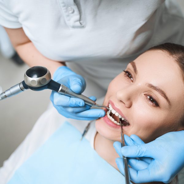 Young female is lying in dental chair during procedures for healing her teeth with equipment